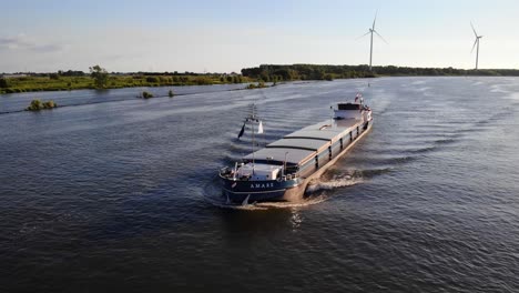 Luftverfolgungsaufnahme-Vom-Bug-Des-Binnenfrachters-Amare,-Der-Vor-Stillstehenden-Windkraftanlagen-Im-Hintergrund-Entlangfährt