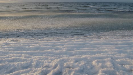 Ice-covered-sea-waves-rolling-in-on-beach-at-golden-hour-sunset