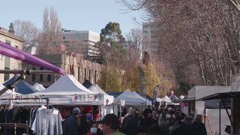 View-up-over-tourists-shopping-and-viewing-stalls-of-iconic-Salamanca-Market-in-Hobart,-Tasmania,-shopping-for-gifts,-scarf,-hat-on-sunny-winter-day