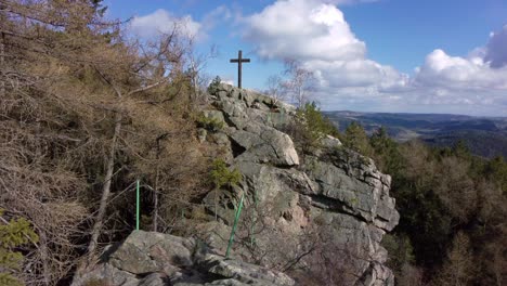 A-wooden-cross-on-a-rocky-peak-towering-over-a-panorama-of-a-spring-landscape-with-forests-in-a-protected-landscape-area-in-the-Czech-Republic