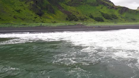 Waves-crashing-on-black-sand-beach-in-Vik,-Iceland-with-drone-over-water-moving-forward