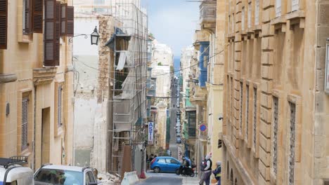 Narrow-long-side-street-of-Valletta-leading-towards-sea,-handheld-view
