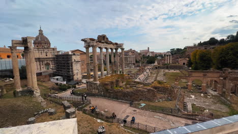 Pov-dolly-forward-showing-old-buildings,-pillars-and-visiting-tourists-at-Roman-Forum-in-Rome