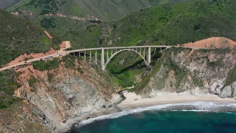 Wide-aerial-view-of-Bixby-Creek-Bridge-on-a-sunny-summer-day-along-Route-1-coastal-road-of-Big-Sur-California-with-the-white-sand-beach-below
