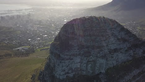 Lens-flare-hazy-city-aerial-retreats-from-Lion's-Head-peak,-Cape-Town