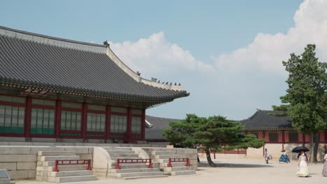 Sujeongjeon-Hall-building-at-Gyeongbokgung-Palace-against-white-clouds-with-tourists-in-hanbok-costumes-walk-by