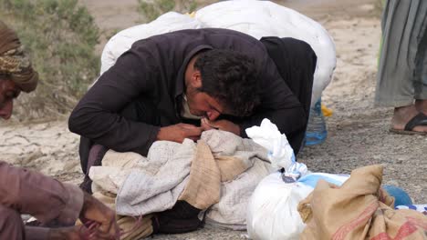 Ein-Ländlicher-Pakistanischer-Mann-Benutzt-Seine-Zähne,-Um-Einen-Kleidersack-Zu-Lösen,-Der-Für-Die-Fluthilfe-In-Belutschistan-Gegeben-Wurde