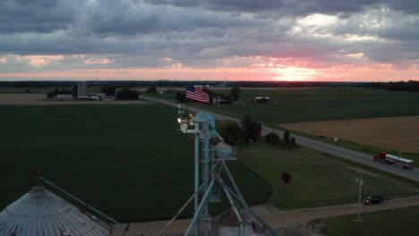 Farm-silo-with-American-flag-waving-on-top-during-sunset-in-rural-Michigan-with-drone-video-moving-out