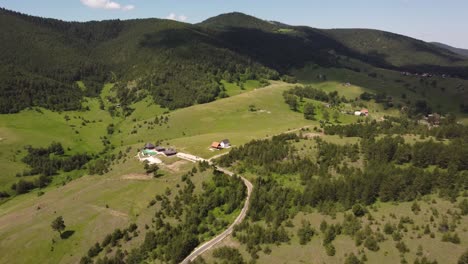 Drone-footage-over-hills-of-mountain-Zlatibor-in-West-Serbia,-nice-flyover-with-houses,-road,-green-pine-forest-and-grass