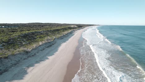 Drone-shot-moving-up-the-coast-of-Magenta-Shores-as-the-waves-crash-along-the-shore