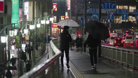 Menschen-Mit-Regenschirmen-Gehen-In-Einer-Regnerischen-Nacht-Mit-Straßenlaterne-In-Tokio,-Japan,-Die-Straße-Von-Shinjuku-Entlang