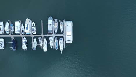 A-moving-drone-view-looking-down-at-multiple-boats-docked-on-a-wharf-in-a-protected-harbor-located-in-the-town-of-Bargara-Bundargerg-Queensland-Australia