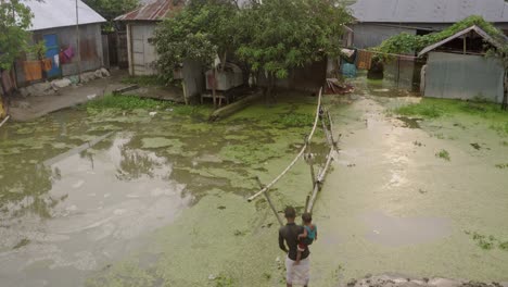 Un-Niño-Lleva-A-Un-Niño-En-Agua-Inundada-Encima-De-Un-Puente-De-Bambú