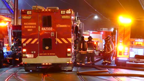 A-group-of-firemen-preparing-to-fight-a-raging-fire-in-between-fire-engines-with-flashing-lights