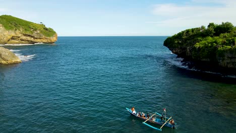 Small-fishing-boat-tourist-trip-in-Gesing-Beach-cove-with-cliffs-aerial-view