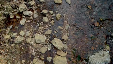 Beautiful-forest-river-with-stones-in-top-down-ascend-drone-view