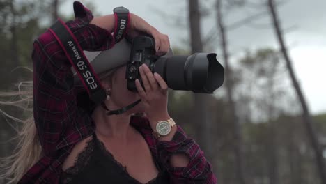 Blonde-Fotografin-Mit-Weißem-Hut,-Die-In-Einer-Sehr-Windigen,-Malerischen-Umgebung-Fotografiert,-Lächelt-Und-Hält-Ihren-Hut,-Als-Würde-Sie-Wegfliegen-–-Filmische-Zeitlupe-–-Canon-Kamera