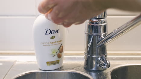Close-up-of-hands-being-washed-with-Dove-soap-by-metallic-kitchen-sink
