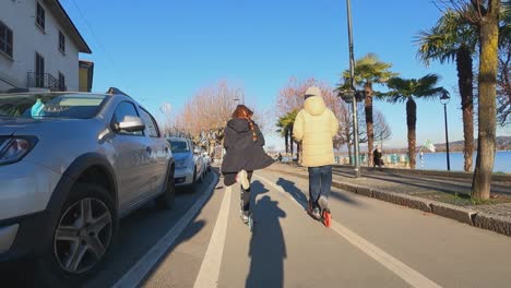 Kids-having-fun-riding-scooter-along-Arona-waterfront-bicycle-lane,-Italy