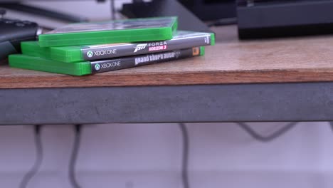 Xbox-One-Konsole-Und-Spiele-Auf-Einem-Tisch,-Mittlere-Einstellung,-Schwenk-Nach-Links