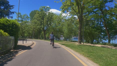 Rückansicht-Einer-Einsamen-Frau,-Die-Fahrrad-Entlang-Der-Uferpromenade-Von-Arona-In-Italien-Fährt