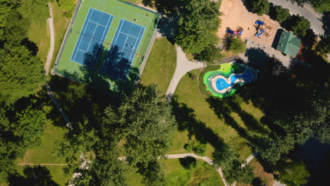 Scenic-aerial-view-over-tennis-courts-and-playgrounds-at-a-city-park-on-a-sunny,-summer-day