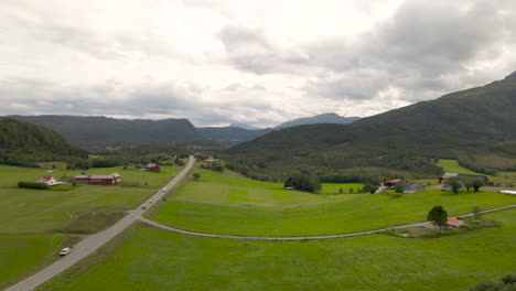 Vista-Pintoresca-Del-Pueblo-Rural-Con-Coches-Que-Viajan-A-Lo-Largo-De-La-Carretera-En-Campos-Verdes-En-La-Costa-Oeste,-Isla-Averoy,-Noruega