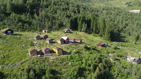 Beautiful-Raksetra-cottages-in-Loen-Norway---Reverse-aerial-with-people-walking-in-lush-nature-during-summer-vacation