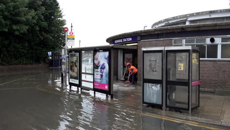 Die-Mitarbeiter-Von-„Transport-For-London“-Wischen-Das-Hochwasser-Vom-Eingang-Der-U-Bahn-Station-Redbridge-Ab,-Nachdem-In-Der-Hauptstadt-Innerhalb-Weniger-Stunden-Heftige-Regenfälle-Im-Ausmaß-Eines-Monats-Zu-Unwettern-Geführt-Hatten