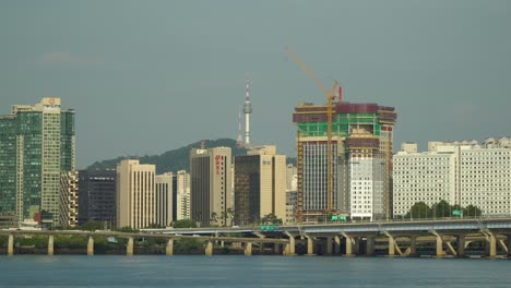 Blick-Vom-Hangang-Fluss-Am-Ufer-Auf-Den-Autoverkehr-Auf-Der-Gangbyeon-Schnellstraße,-Die-Mapodaegyo-Mapo-Brücke-Und-Die-Skyline-Der-Stadt-Mapo-Gu-Mit-Dem-Wahrzeichen-Seouls,-Dem-Namsan-Turm-über-Blauem-Himmel