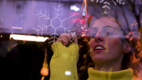 Woman-drawing-a-snow-flakes-on-the-window-of-a-bar-for-Christmas-decoration