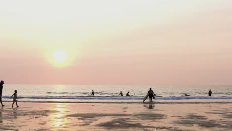 Surfer-Mit-Surfbrettern-Geht-Bei-Sonnenuntergang-Am-Sandstrand-Zum-Meer
