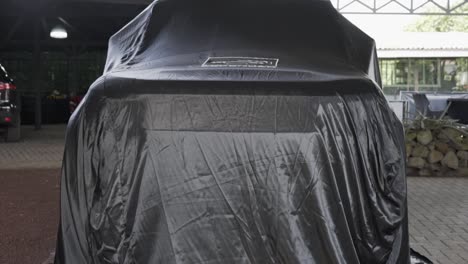 Land-rover-Defender-new-generation,-British-off-road-car,-covered-with-black-tarpaulin-to-give-a-surprise