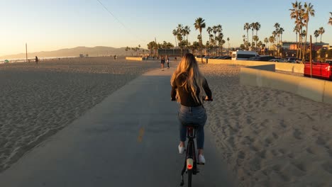 Mujer-Montando-En-Bicicleta-En-El-Carril-Bici-En-Venice-Beach-Al-Atardecer,-California