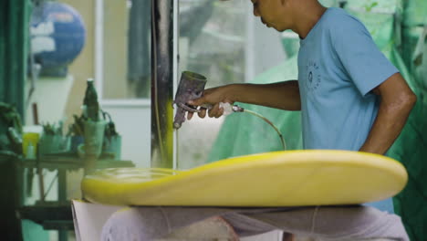 Handyman-finishes-paint-job-on-surfboard-using-spray-gun-with-yellow-acrylic-paint