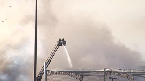 Firefighters-on-ladder-spray-water-on-fire