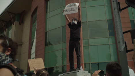 Protestor-holding-up-a-sign-that-says-no-justice-no-peace-during-a-protest-by-the-City-Hall-on-a-sunny-day