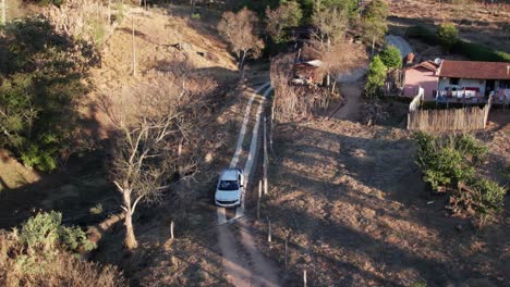 Aerial-footage-of-a-white-car-driving-down-on-a-rural-off-road-trail-and-stops-in-front-of-a-gate