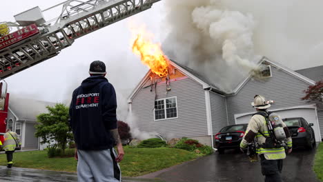 A-Bystander-Watches-as-Flames-Shoot-out-of-the-Roof-of-a-Burning-Home-in-the-Rain