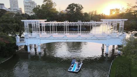 High-angle-static-shot-overlooking-at-paddle-boat-sailing-pass-greek-inspired-white-quaint-bridge-at-downtown-urban-botanical-garden-Paseo-El-Rosedal,-Palermo-Woods,-Buenos-Aires