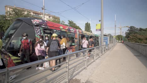 People-boarding-a-dark-painted-tramway-wearing-masks-during-the-pandemic,-Walking-forward-shot