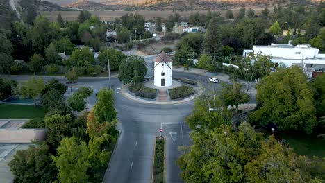 Aerial-dolly-out-of-Leonidas-Montes-windmill-in-roundabout-with-cars-driving-surrounded-by-trees,-hills-in-background,-Lo-Barnechea,-Santiago,-Chile