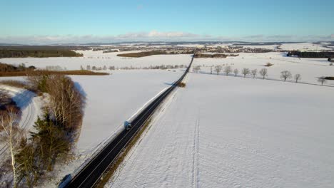 Aerial-Drone-Panning-Across-Winter-Snow-Landscape-Above-Cars-On-Rural-Road-Towards-Distant-City-Of-Svitavy-In-Czech-Republic-On-Sunny-Day-With-Blue-Sky