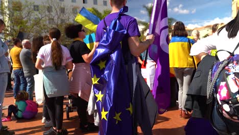 Langsamer-Schwenk-über-Einen-Mann,-Der-Während-Der-Antikriegsproteste-Die-EU-Flagge-Auf-Dem-Rücken-Trägt