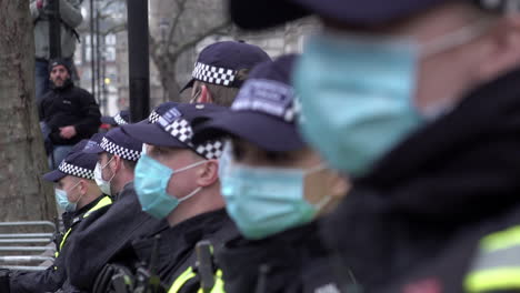 Eine-Einheit-Großstadtpolizisten-Mit-Schützenden-Chirurgischen-Gesichtsmasken-Sowie-In-Schwarzen-Uniformen-Und-Blauen-Mützen-Steht-In-Einer-Reihe-Und-Bildet-Eine-Absperrung