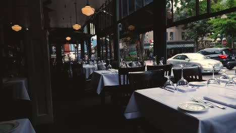 fine-Dining-tables-set-for-lunch-or-dinner-at-fancy-restaurant-Water-street-cafe-ceramic-plates-forks-knives-cloth-napkins-on-white-tablecloth-table-Steady-Slow-motion-tilting-right-revealing-room