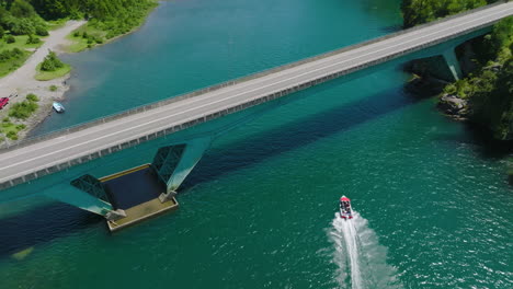 Aerial-Over-Speed-Boat-Along-Puelo-River-Going-Under-Low-Bridge-In-Chile,-Lake-District