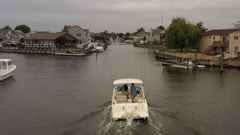 An-aerial-view-of-a-fishing-boat-sailing-through-a-canal-behind-houses-on-Long-Island-on-a-cloudy-day