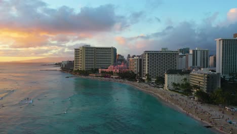 Olas-De-Surf-Cerca-De-Los-Edificios-Del-Hotel-Resort-Frente-Al-Mar-Y-Turistas-Nadando-En-La-Playa-De-Kuhio-En-Waikiki,-Hawaii-Al-Atardecer