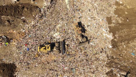 Birds-flying-over-landfill-with-industrial-equipment-on-top,-aerial-top-down-view
